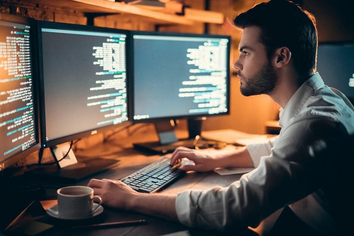 Programmer Coding on Computer with Three Monitors